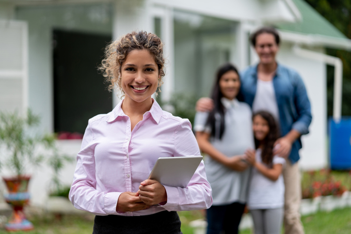 Portrait of a real estate agent showing a family a suburb house and looking at the camera smiling
