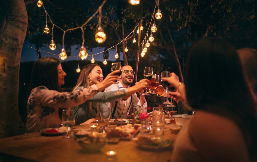 group of friends making a toast with wine, on a picnic table with lights hanging above them